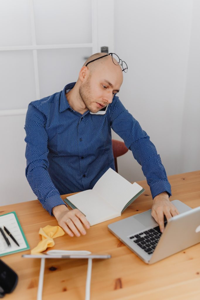 A multitasking male. Phone on shoulders/ears, laptop, tablet, and notebook.